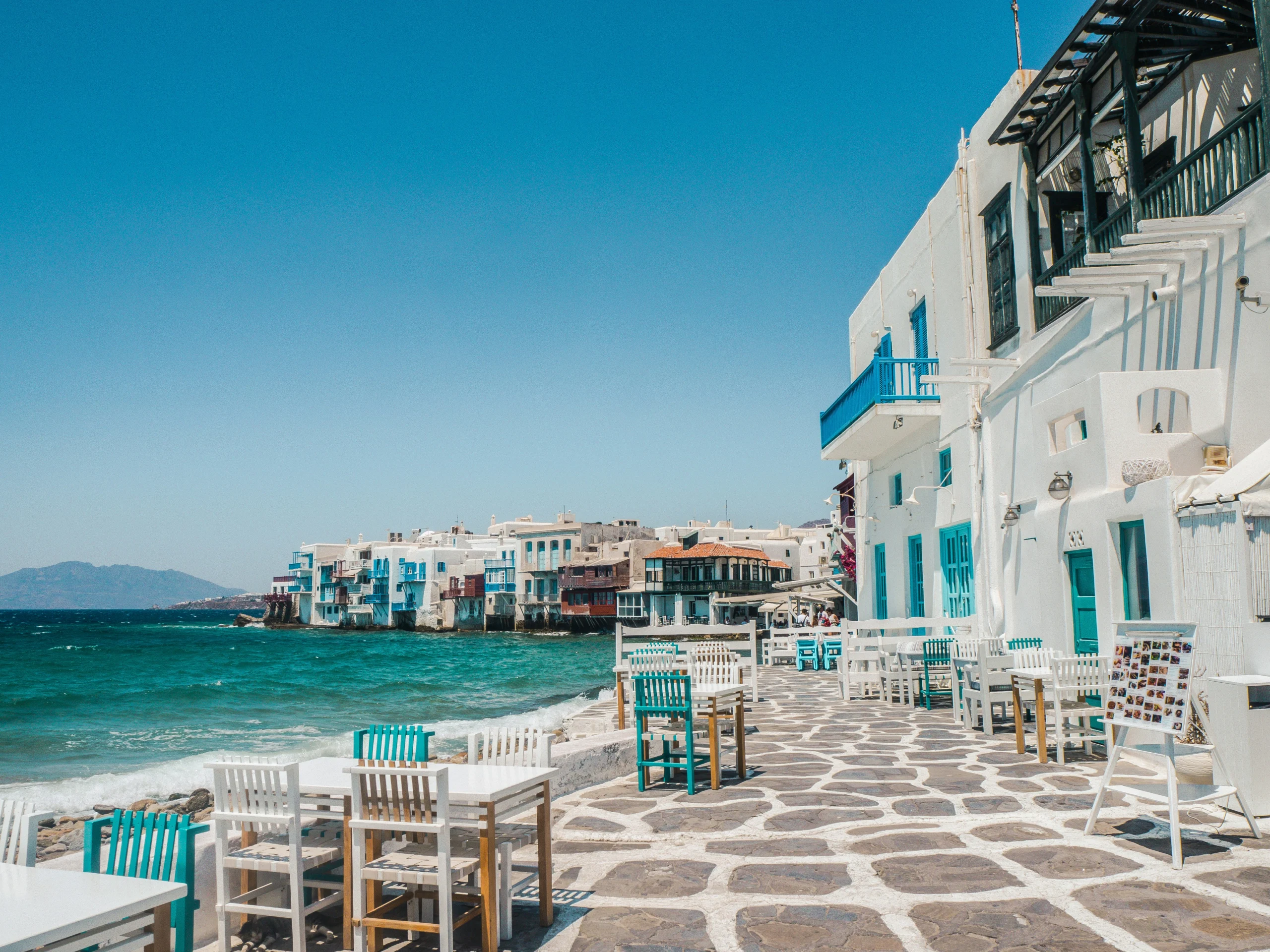 waterside chairs with whitewashed buildings and turquoise water in Mykonos