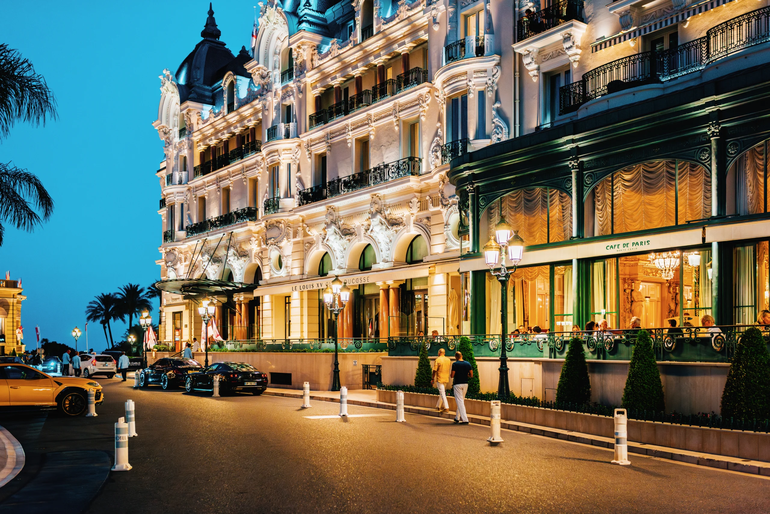 A glamorous evening view of the Hôtel de Paris and Café de Paris in Monte Carlo, Monaco, illuminated by elegant lighting.