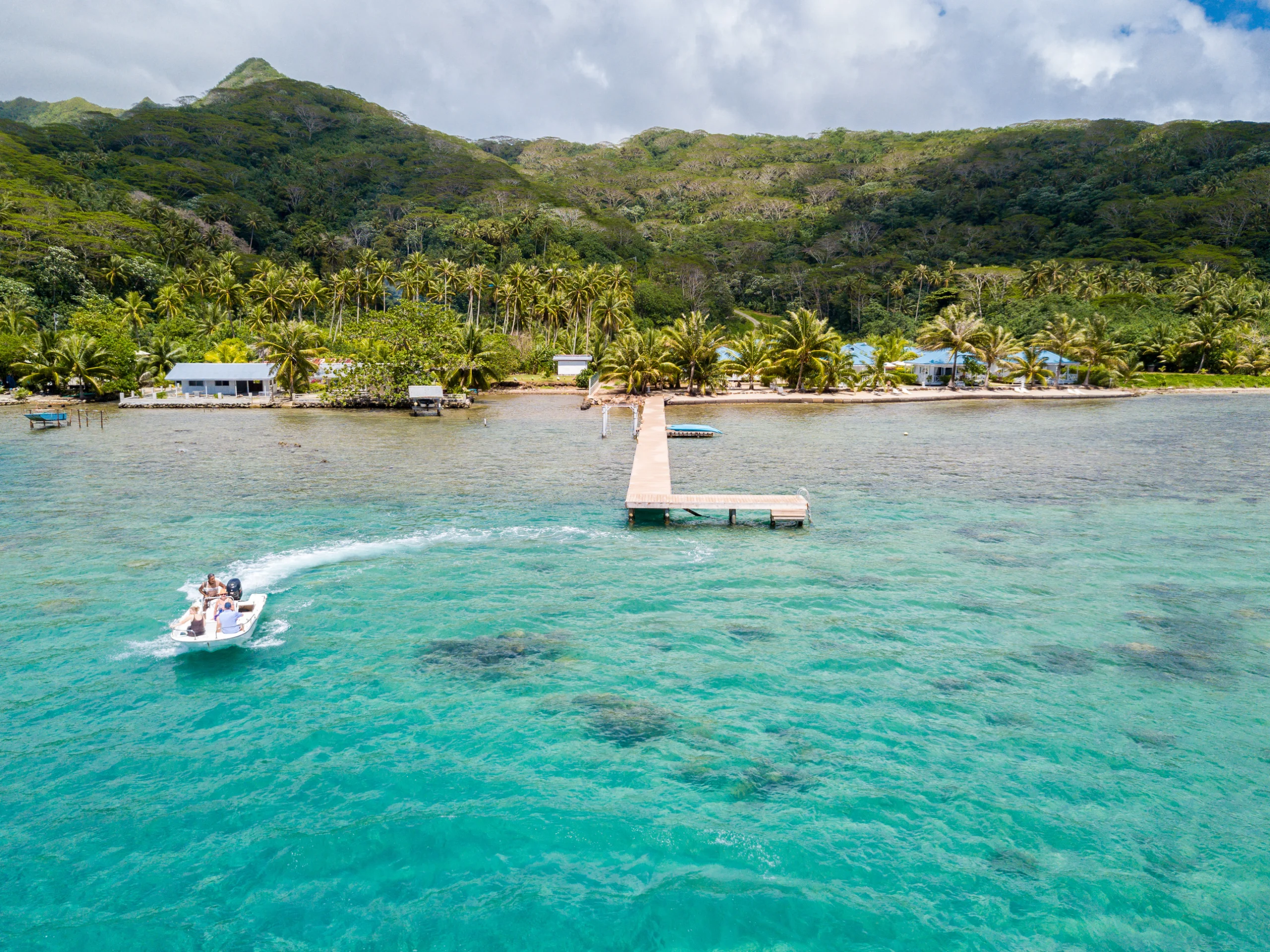 Tourists riding high speed jet boat in a stunning azure blue turquoise lagoon, green emerald island in back