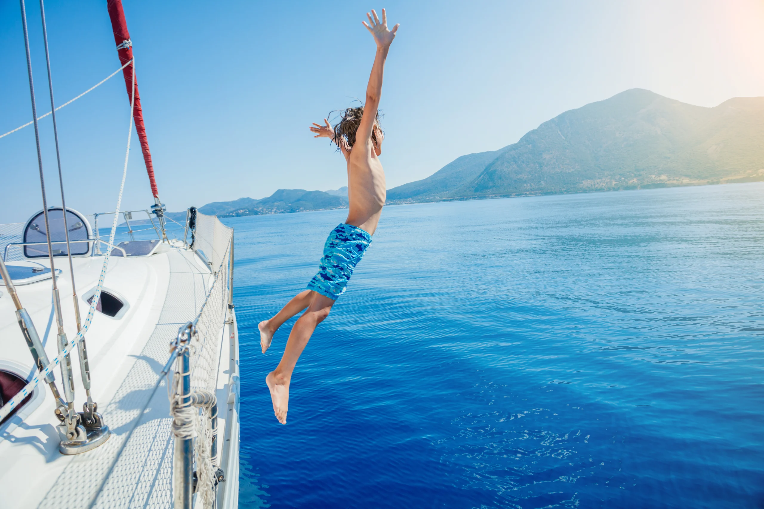 Boy jump of sailing yacht on summer cruise