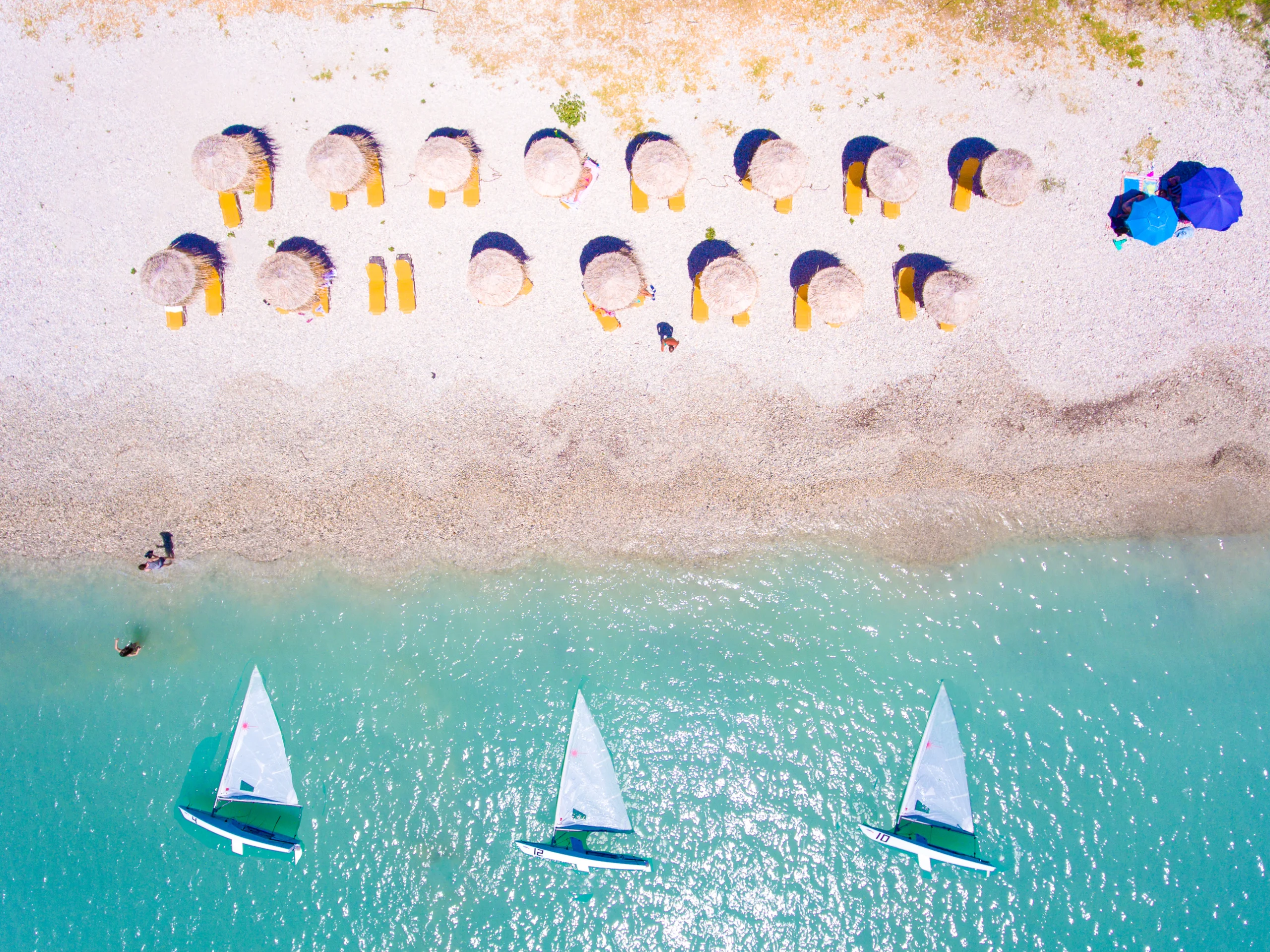 Summer beach in Lefkada Greece with sun umbrellas and sunbeds and yachts in the water aerial view