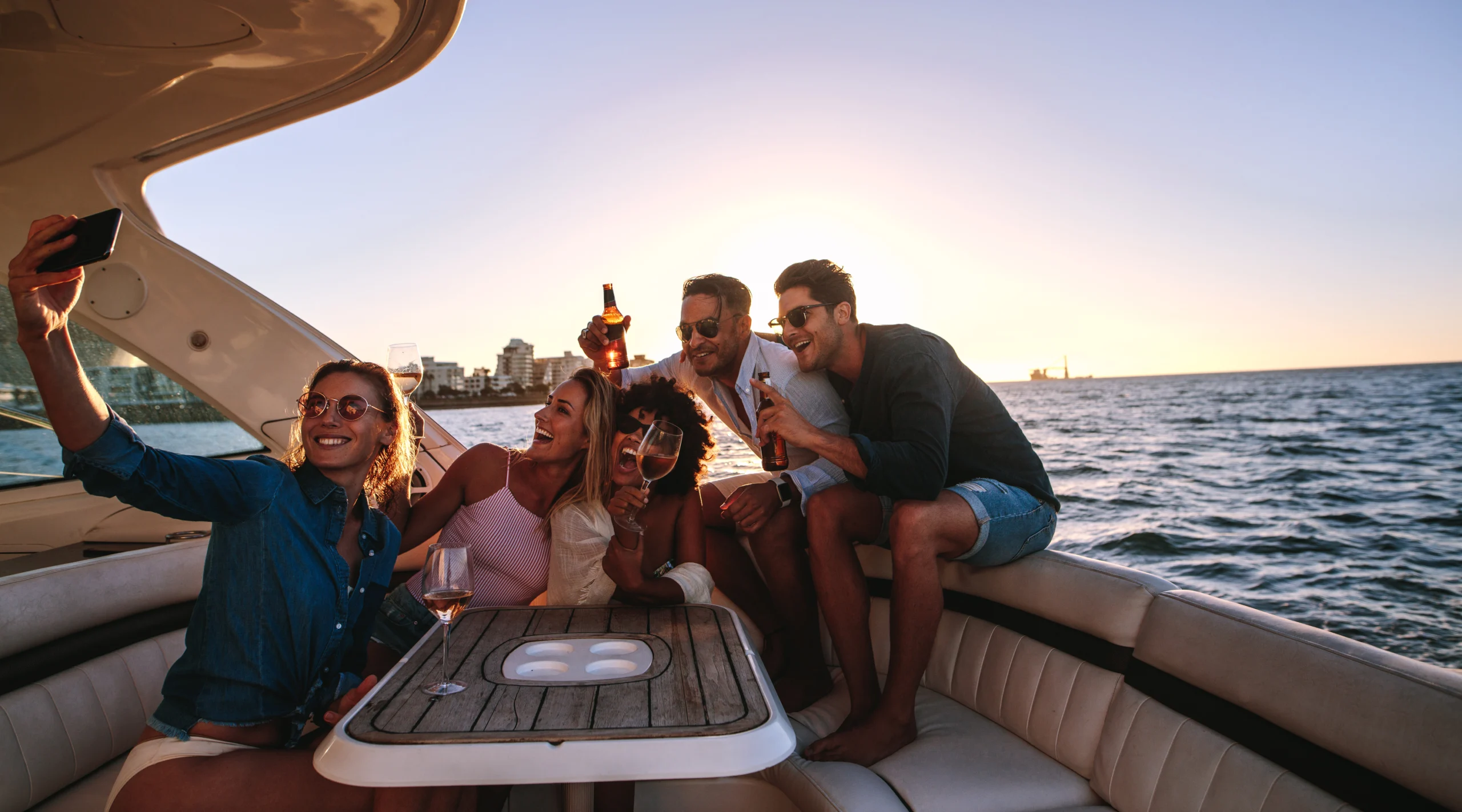 Group of men and women relaxing on the yacht with drinks and taking selfie.