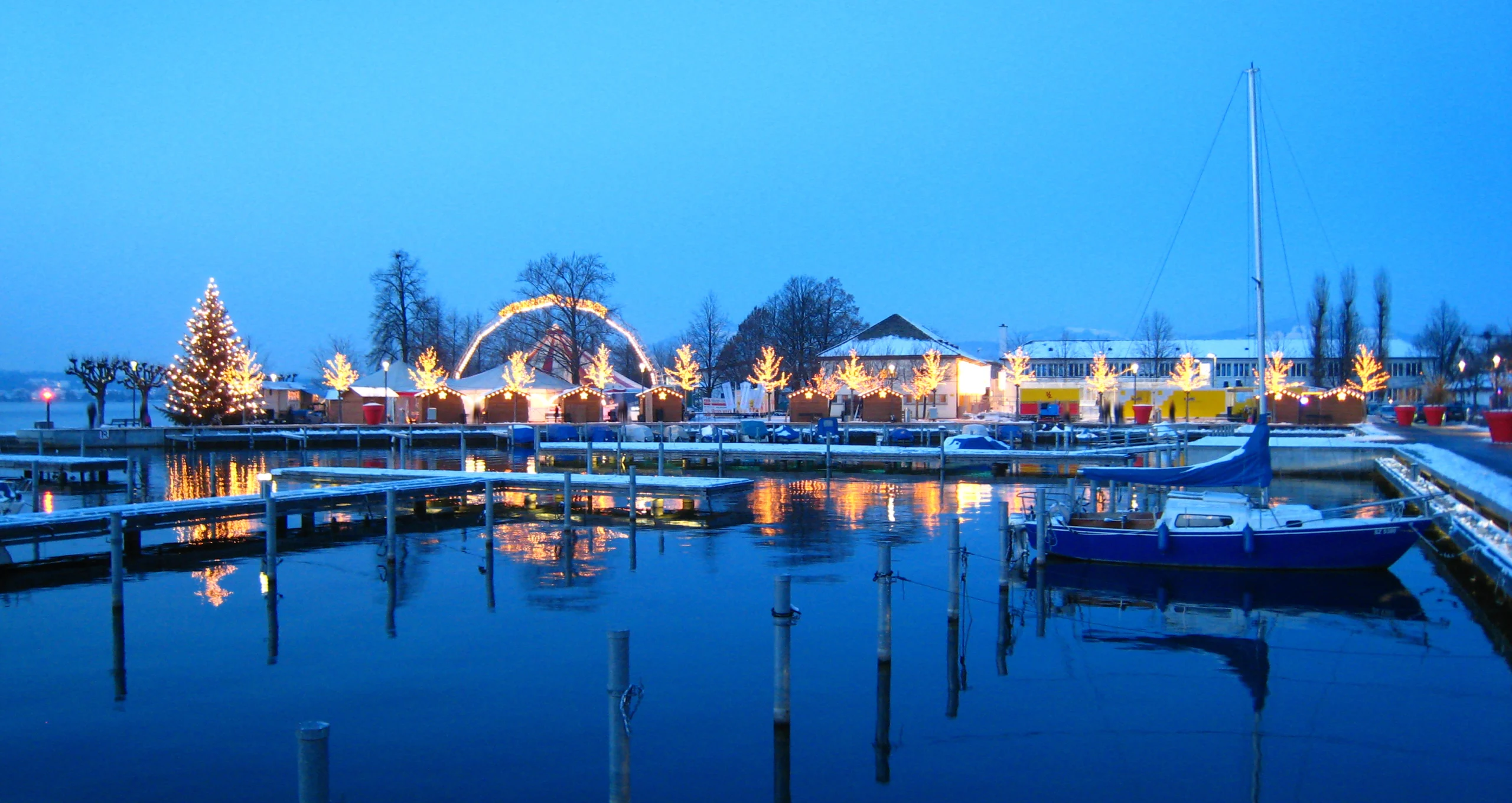 Beautiful swiss christmas market in switzerland on the lake shore with snow covered ships at the harbor