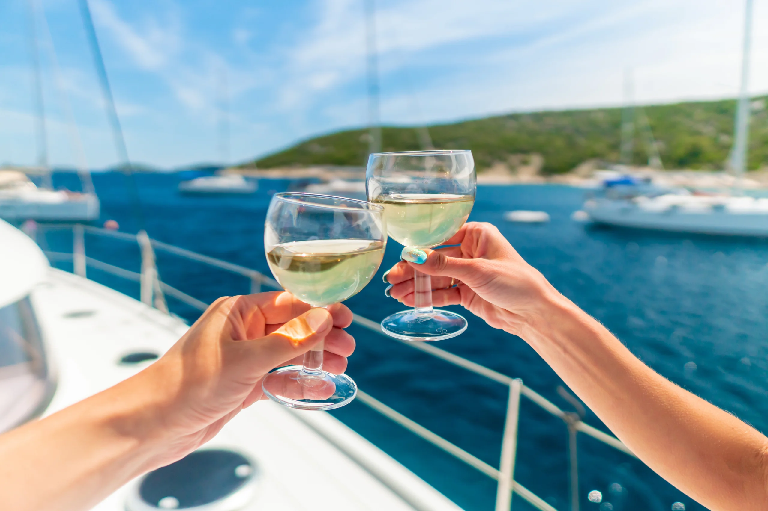Couple holding two glasses of white wine over ocean background with yacht on background