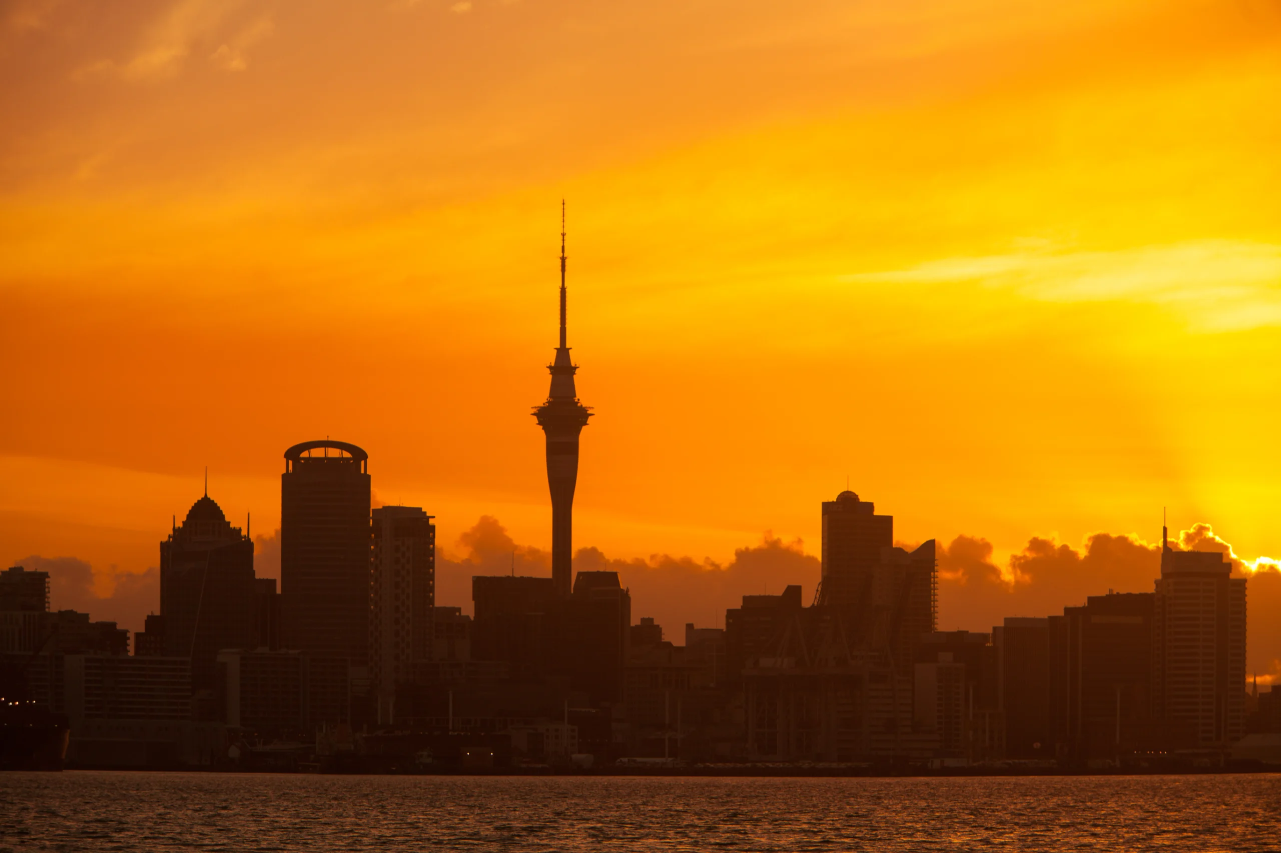 Auckland, New Zealand skyline at sunset with vibrant orange sky and silhouetted buildings