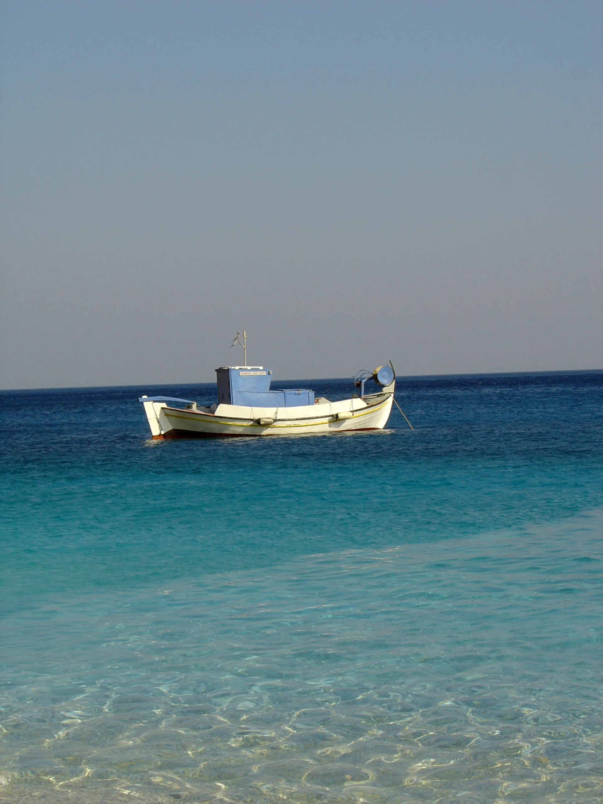 A small fishing boat in the light blue sea