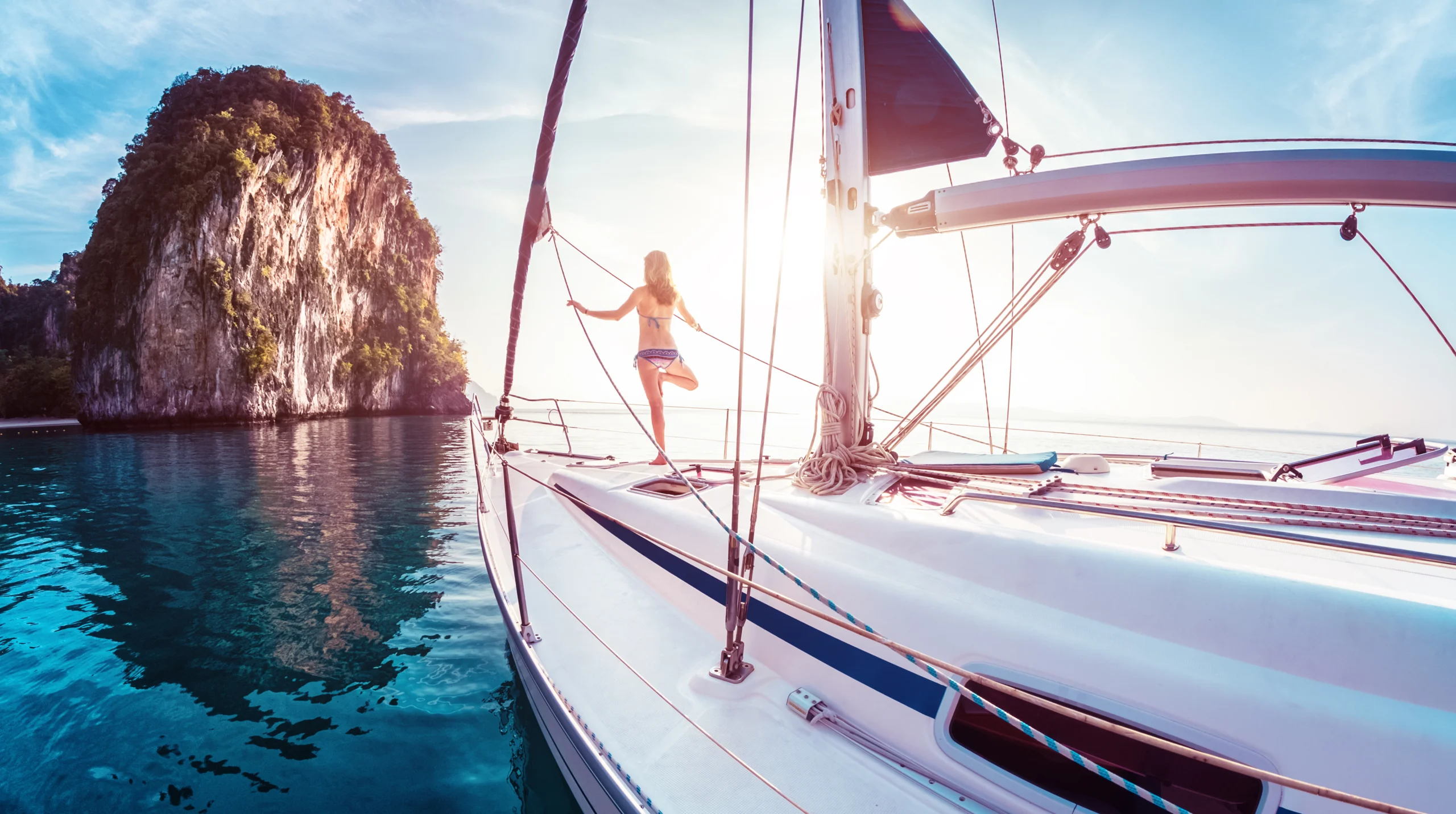 Young lady standing on the bow of yacht and doing exercise at sunrise