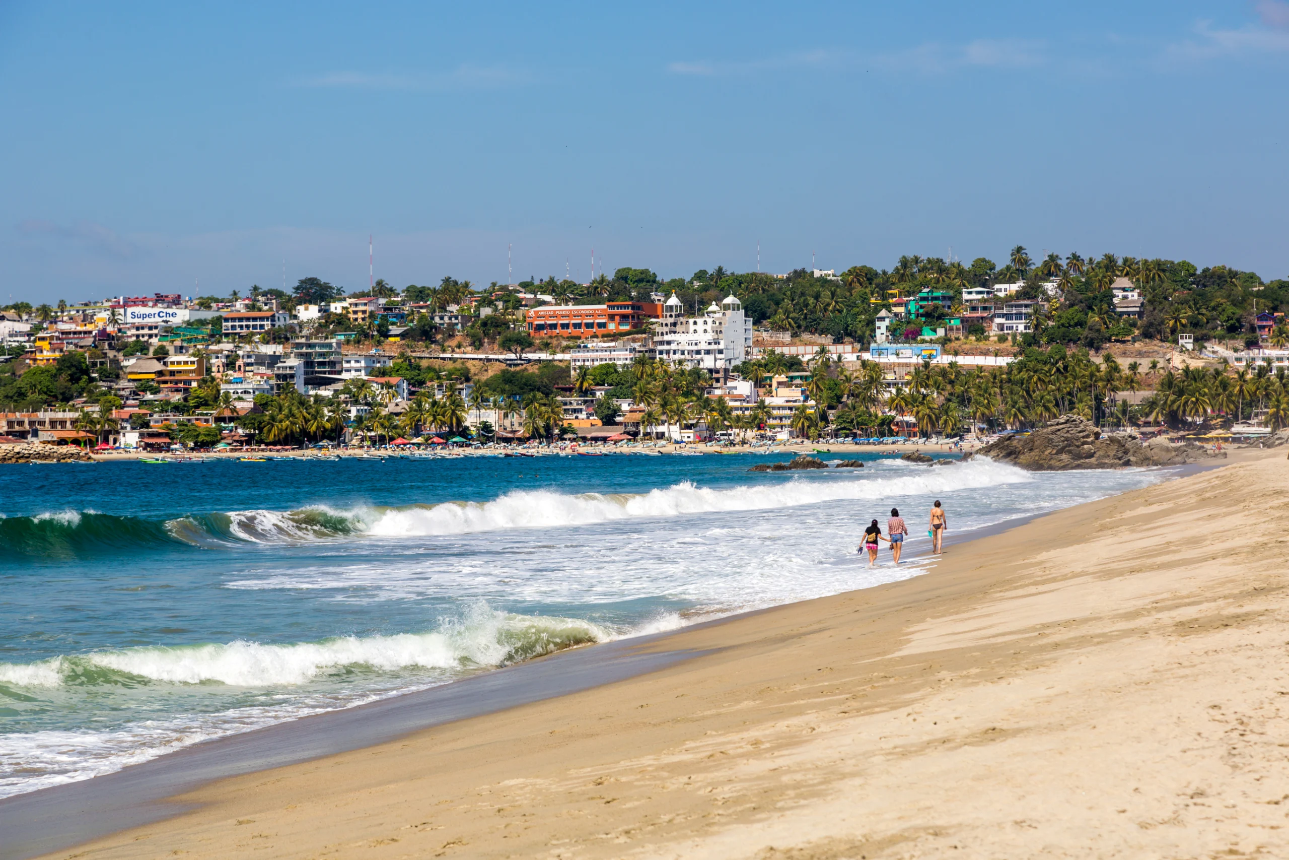 People walking on Puerto Escondido beach, with a nice green forest in the background, Mexico