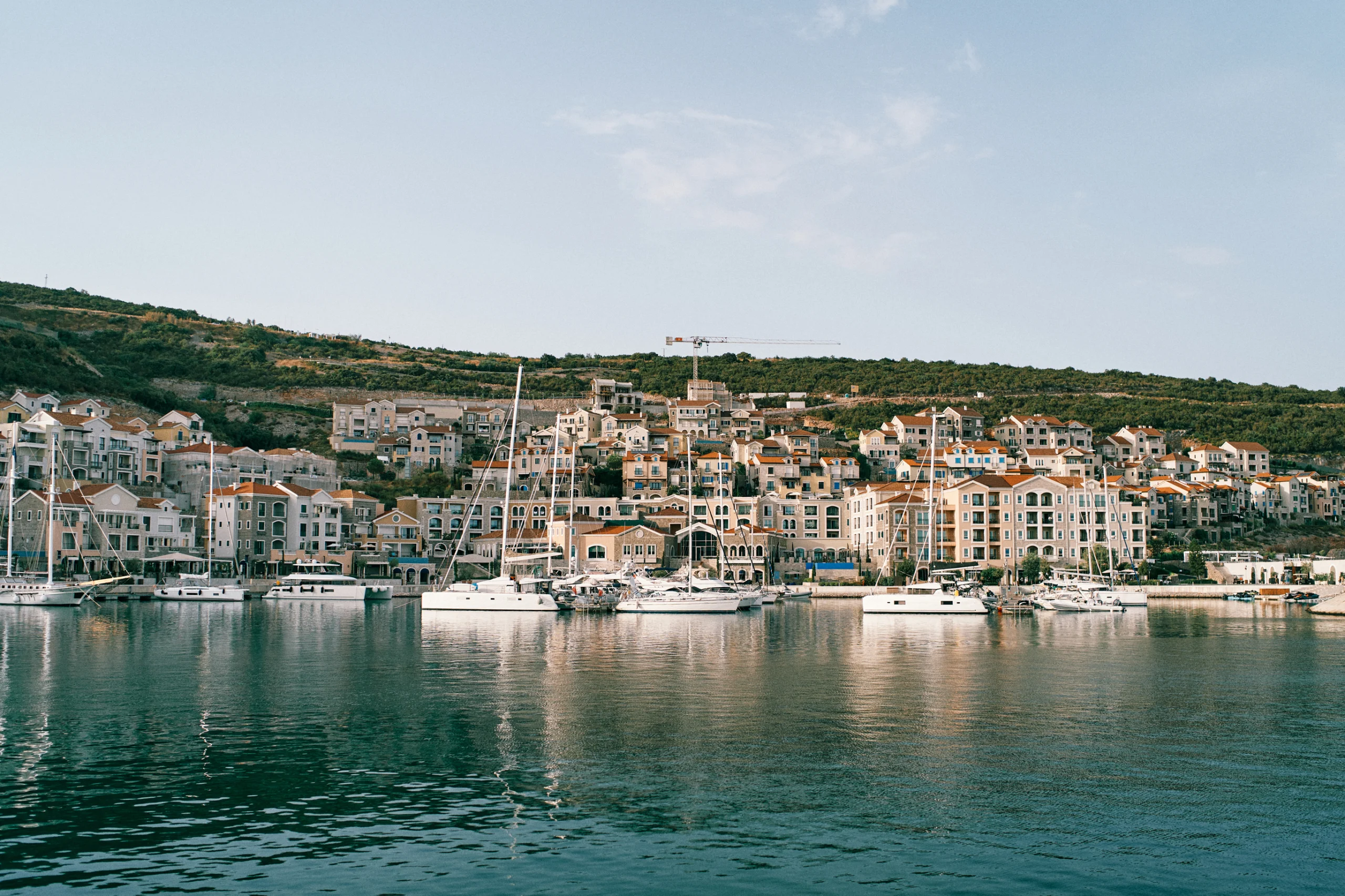 Sailing yachts are moored off the coast of a bay with colorful houses