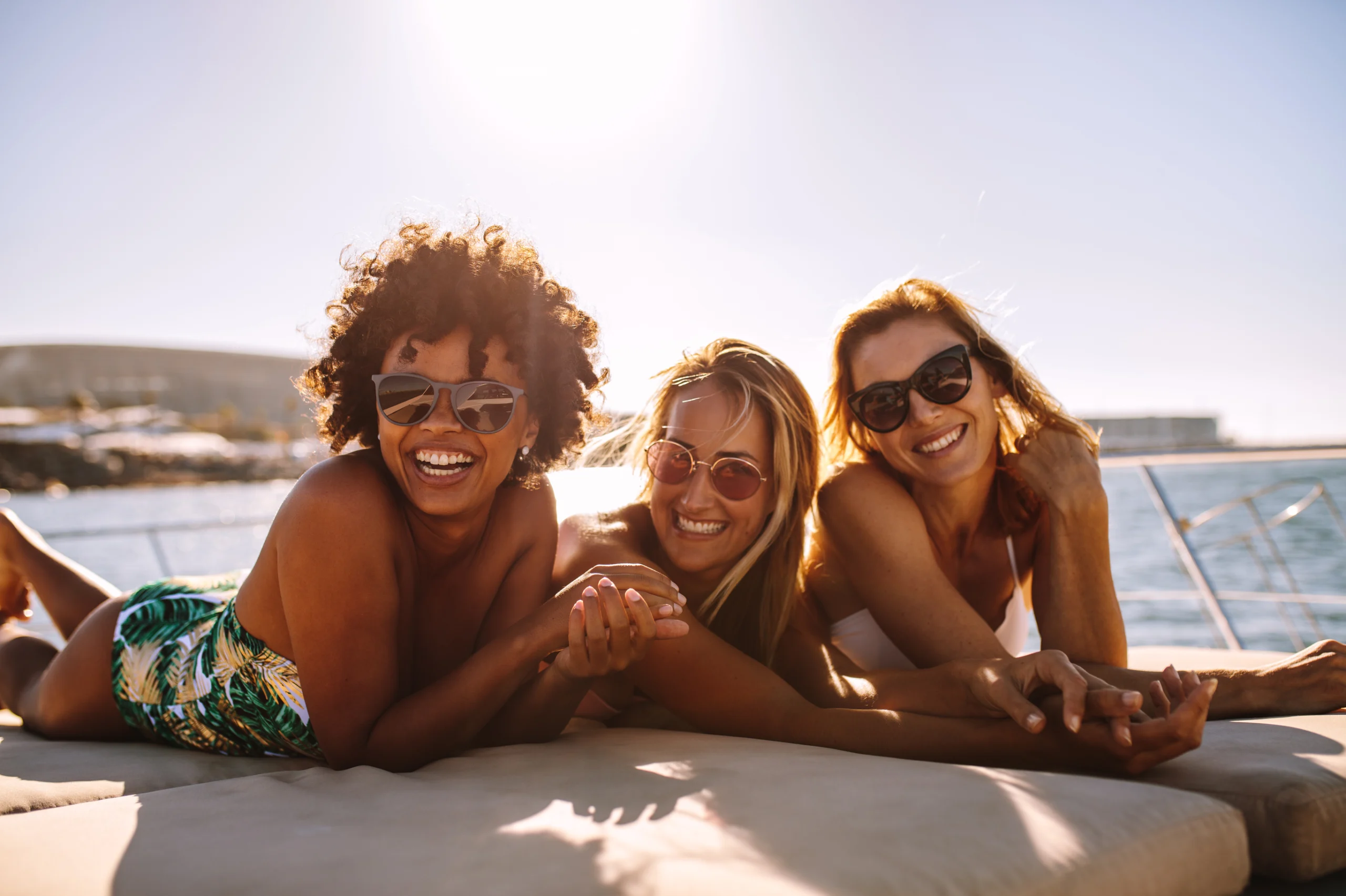 Cheerful women sunbathing on private yacht. Multiracial group of females wearing sunglasses lying on the bow of a yacht on a summer day. Three young women sunbathing on private yacht.