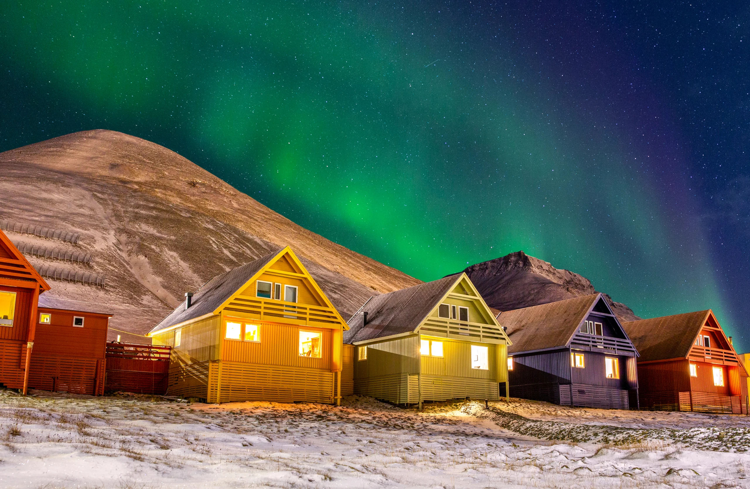Longyearbyen colorful houses with Aurora Borealis in the sky full of stars. Photograph taken in November 2019 during the polar night in the northenmost town in the world - Longyearbyen, Norway. The aurora was dancing above my head for few minutes and then disappeared behind the hills. Wonderful show nature can let us see in this cold land.